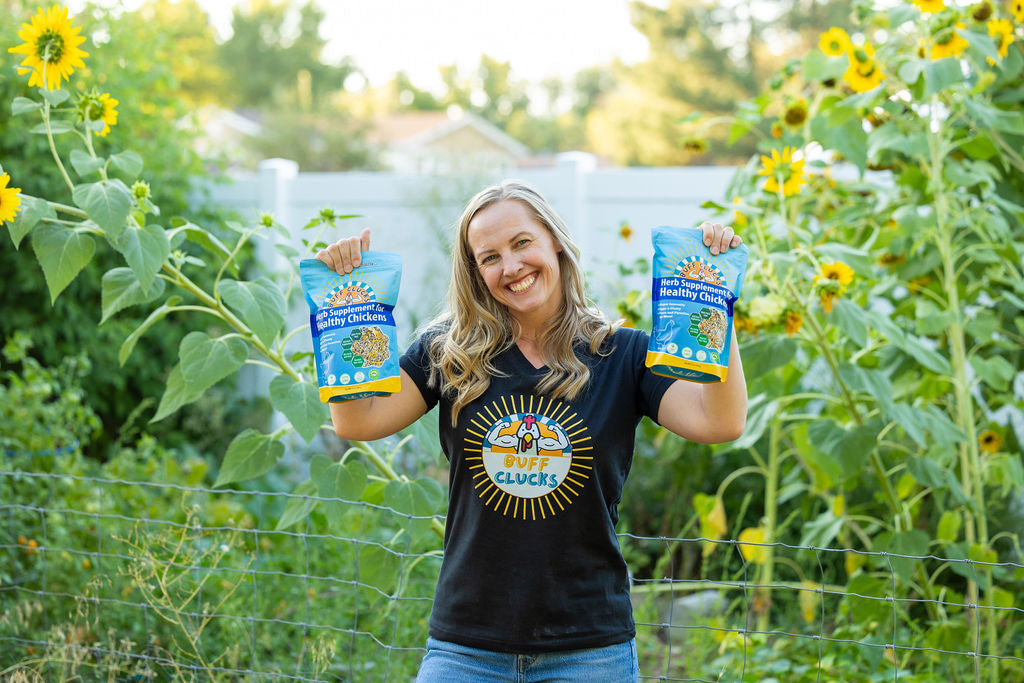 woman holding 2 bags of buff clucks herb supplement for chickens with sunflowers in back