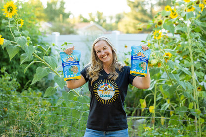woman holding 2 bags of buff clucks herb supplement for chickens with sunflowers in back